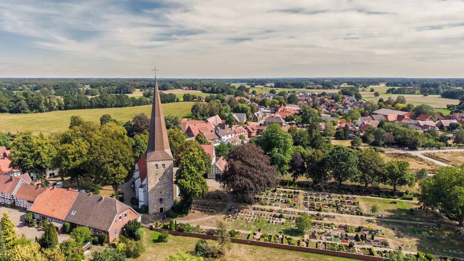 Drohnenaufnahme vom Ortskern Menslage mit Kirchturm, Fachwerkhäusern und den Feldern des Artlands